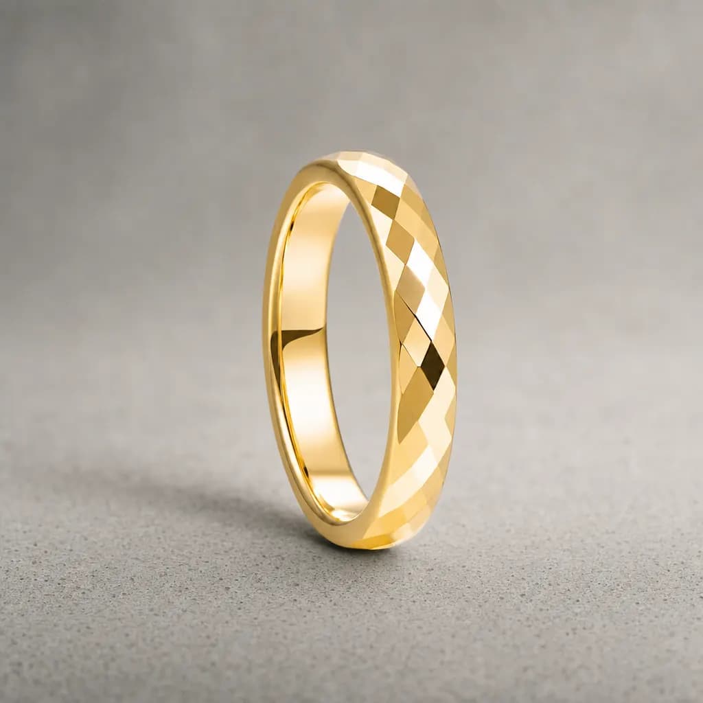The Anvil, a 4mm faceted gold tungsten carbide band, standing upright on a poured concrete ledge