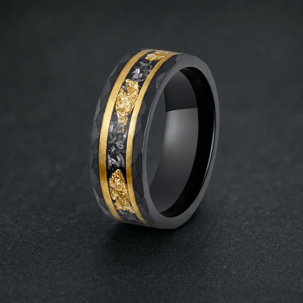 The Halley, an 8mm hammered tungsten carbide band in black and gold with a meteorite inlay, standing upright on a dark iron grey stone slab