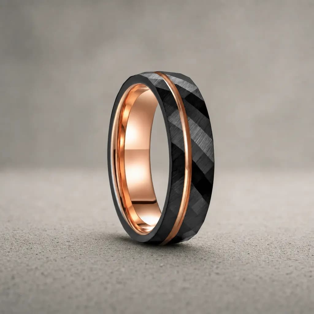 The Peen, an 8mm faceted tungsten carbide band in black and rose gold, standing upright on a poured concrete ledge