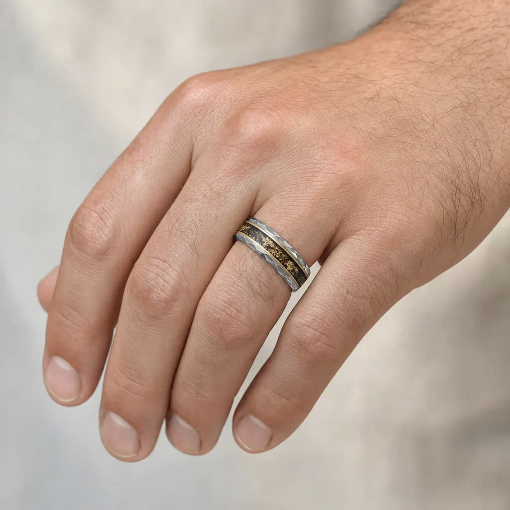The Perseid, an 8mm faceted tungsten carbide band in silver, gold and black with a meteorite inlay, worn on the hand