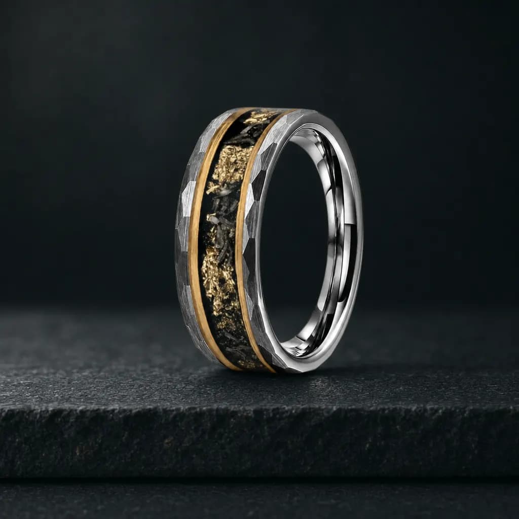 The Perseid, an 8mm faceted tungsten carbide band in silver, gold and black with a meteorite inlay, standing upright on a dark iron grey stone slab
