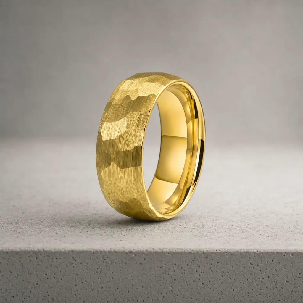 The Relic, an 8mm hammered gold tungsten carbide band, standing upright on a poured concrete ledge