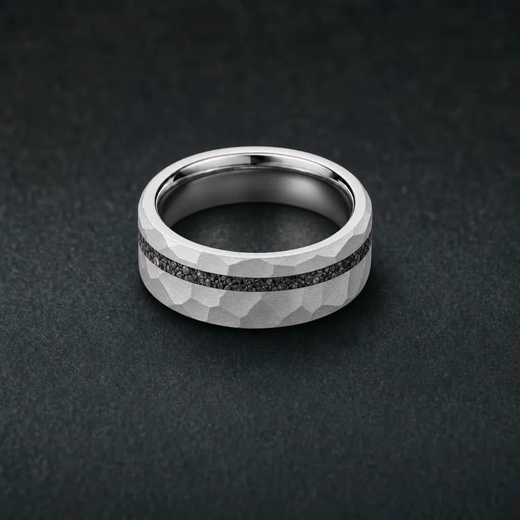 The Vulcan, an 8mm hammered silver tungsten carbide band with a meteorite inlay, lying flat on a dark iron gray stone slab