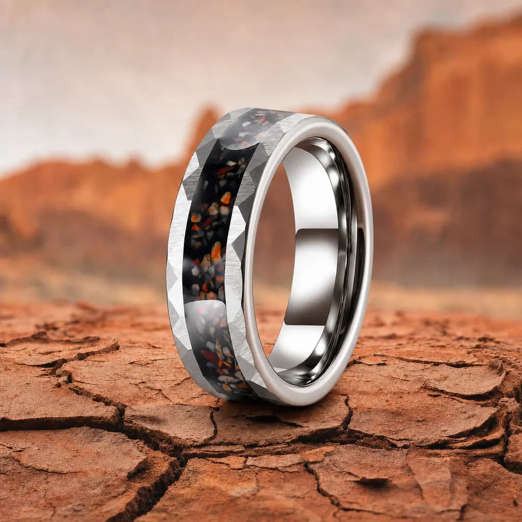 The Fossil, an 8mm faceted tungsten carbide band in silver and black with a dinosaur bone inlay, standing upright on cracked red desert earth