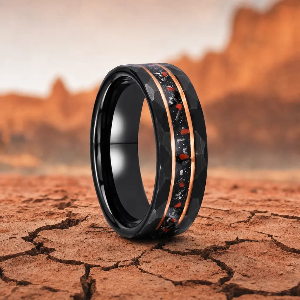 The Quarry, an 8mm faceted tungsten carbide band in black and rose gold with a dinosaur bone inlay, standing upright on cracked red desert earth