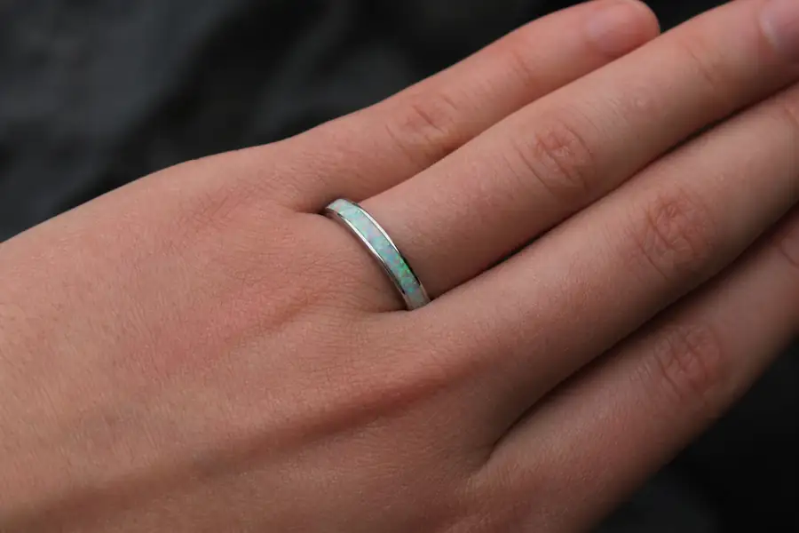 An opal band on a hand against a dark background